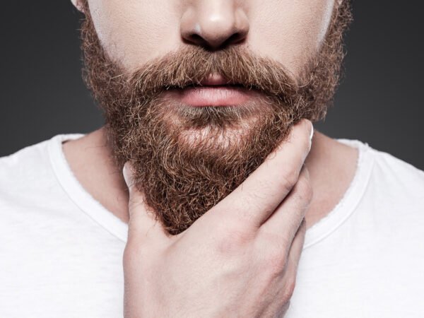 Touching his perfect beard. Close-up of young bearded man touching his beard while standing against grey background